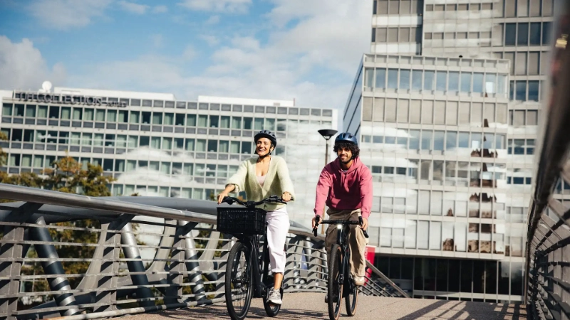 Zwei Radler:innen fahren auf einer Brücke mitten in der Stadt bei schönem Wetter