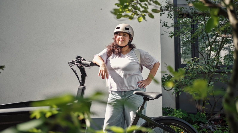 Eine Frau lehnt stolz an ihrem Lastenrad und trägt einen Helm.