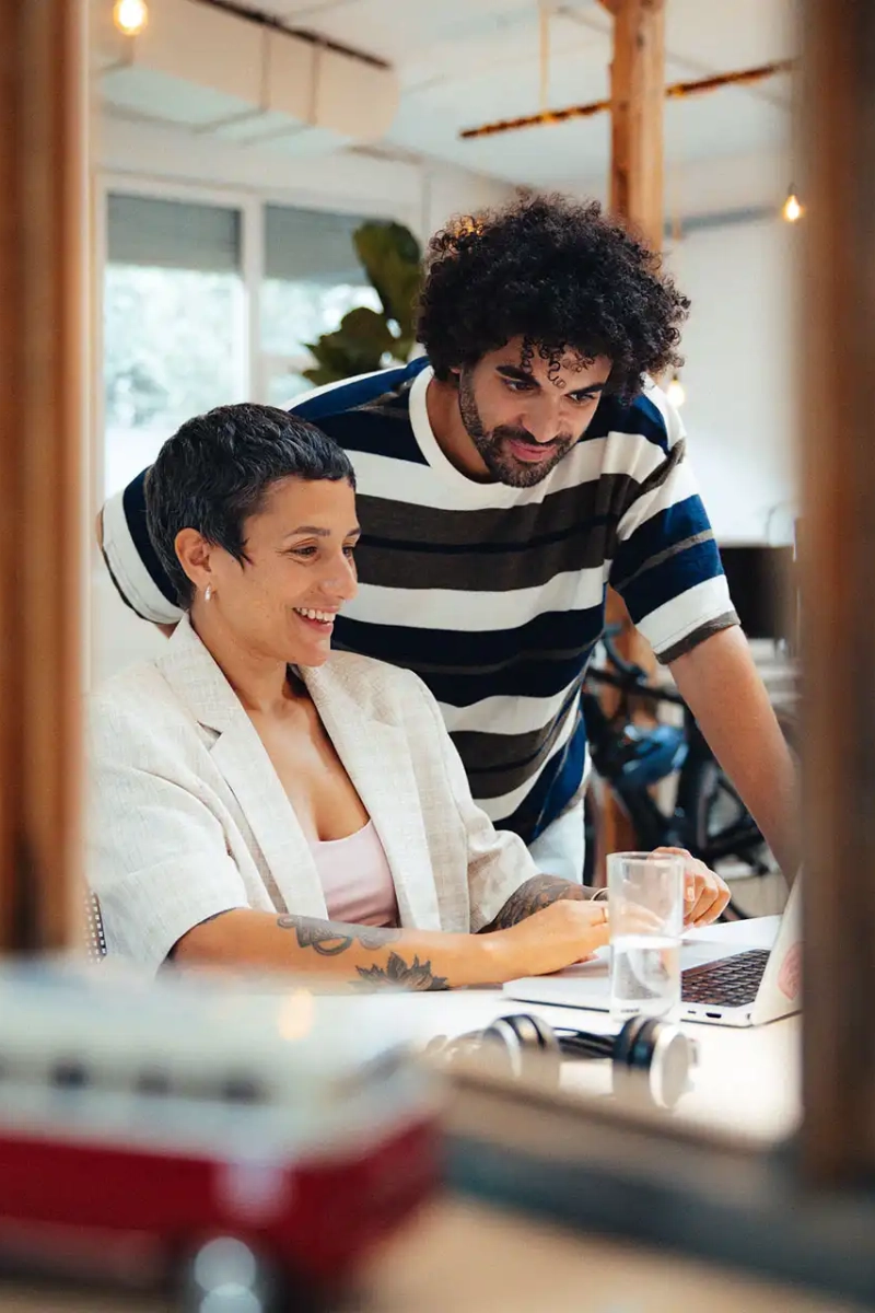 Mitarbeitende schauen begeistert zusammen auf Laptop im Büro