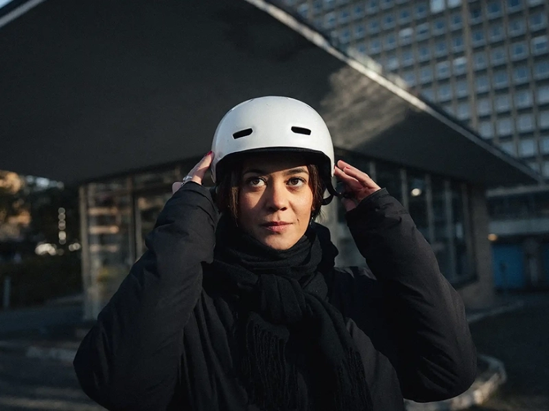 Eine junge Arbeitnehmerin setzt sich ihren Fahrradhelm auf.