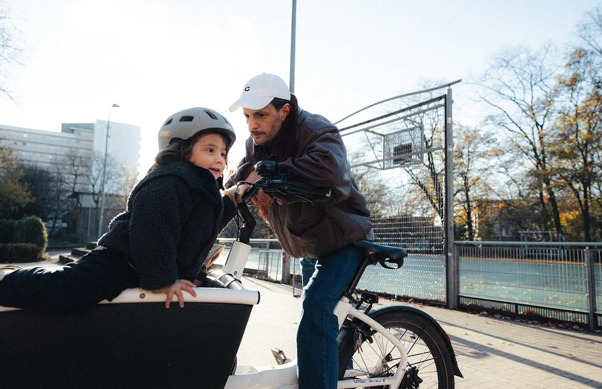 Vater spricht mit Sohn vorne übergebeugt im weißen Lastenrad